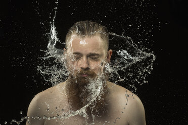 Wasser spritzt auf das Gesicht eines Mannes ohne Hemd vor schwarzem Hintergrund - FSIF02301