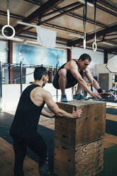 Männlicher Sportler, der einem Freund beim Boxspringen im Fitnessstudio hilft - FSIF02305