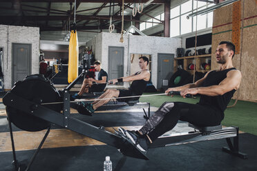 Entschlossene Männer trainieren an Rudergeräten im Fitnessstudio - FSIF02306