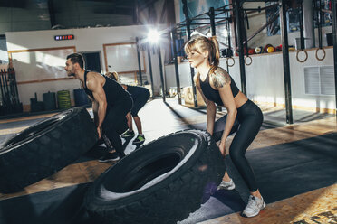 Determined male and female athletes flipping tire at health club - FSIF02312