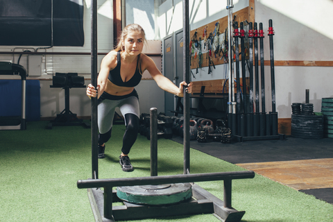 Entschlossene Frau bei der Schlittenschiebeübung im Fitnessstudio, lizenzfreies Stockfoto