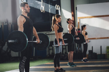 Side view of male and female athletes lifting barbells at health club - FSIF02317