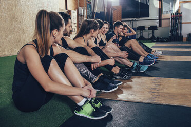 Männliche und weibliche Sportler unterhalten sich auf einem Teppich im Fitnessstudio - FSIF02318