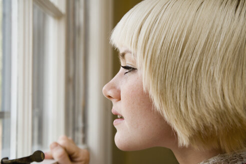 Junge Frau schaut aus einem Fenster - FSIF02340