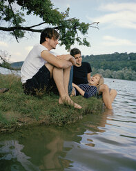 Three friends sitting at the edge of a lake - FSIF02360