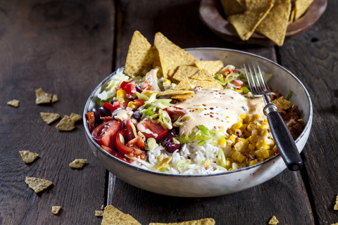 Taco salad bowl with rice, corn, chili con carne, kidney beans, iceberg lettuce, sour cream, nacho chips, tomatoes stock photo