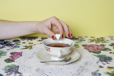 Die Hand einer Frau lässt einen herzförmigen Zuckerwürfel in eine Tasse Tee fallen - FSIF02496