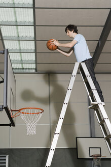 A Young Man standing on a ladder preparing to drop a basketball into a basketball hoop - FSIF02517