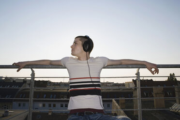 A young man sitting on a rooftop wearing headphones - FSIF02522