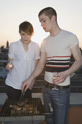 Ein junges Paar beim Grillen auf einer Dachterrasse - FSIF02523