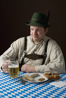 Stereotypical German man in Bavarian costume with a beer and German meal - FSIF02547