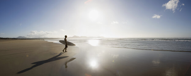 A young man standing on a beach and carrying a surfboard - FSIF02564