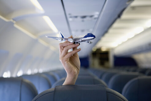 Eine Hand hält ein Spielzeugflugzeug über einem Flugzeugsitz - FSIF02597