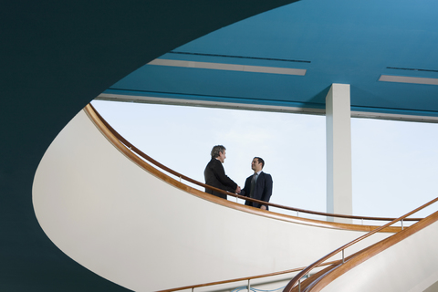 Two businessmen standing on a balcony and shaking hands stock photo