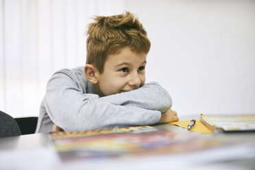 Grinning schoolboy leaning on desk in class - ZEDF01196