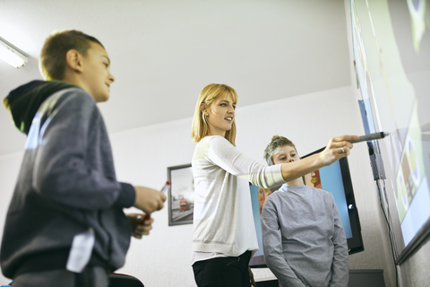 Teacher with students in class at interactive whiteboard stock photo