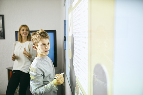 Schüler im Unterricht am interaktiven Whiteboard mit Lehrer im Hintergrund, lizenzfreies Stockfoto