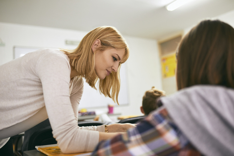 Teacher helping student at desk in class stock photo