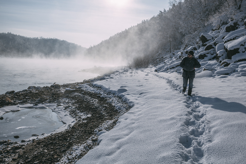 Russia, Amur Oblast, man walking at riverside of Bureya in snow-covered nature stock photo