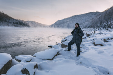 Russia, Amur Oblast, man standing at riverside of Bureya in winter - VPIF00316