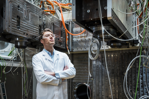 Man wearing lab coat and safety goggles looking at machine stock photo