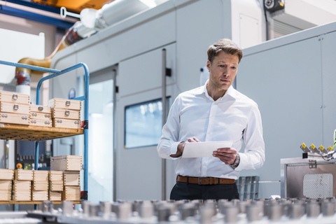 Businessman in factory holding tablet looking at machine stock photo
