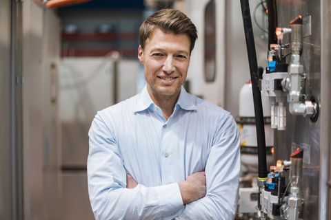 Porträt eines lächelnden Geschäftsmannes an einer Maschine in einer Fabrik, lizenzfreies Stockfoto