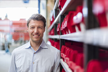 Portrait of smiling man at shelf in factory storeroom - DIGF03426