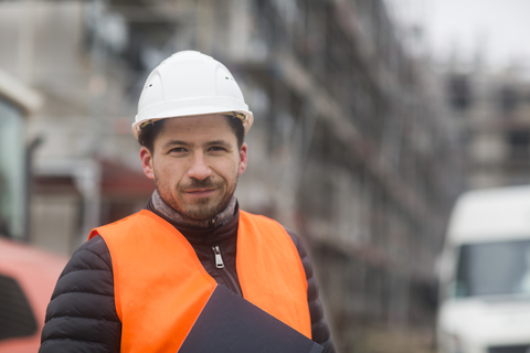 Porträt eines zufriedenen Mannes mit Sicherheitsweste und Helm auf einer Baustelle, lizenzfreies Stockfoto