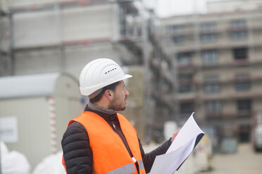 Mann mit Plan trägt Sicherheitsweste und Schutzhelm auf einer Baustelle - SGF02190