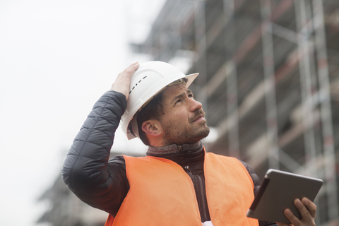 Man with tablet wearing safety vest and hard hat at construction site stock photo