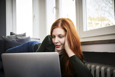 Porträt einer rothaarigen Frau, die zu Hause einen Laptop benutzt - FMKF04861