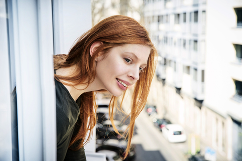 Porträt einer lächelnden rothaarigen Frau, die sich aus dem Fenster lehnt, lizenzfreies Stockfoto