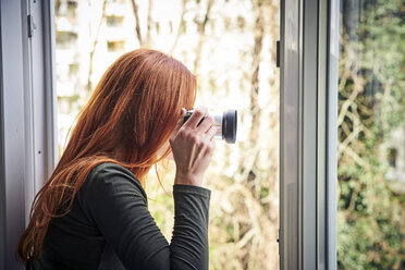 Rothaarige Frau lehnt sich aus dem Fenster und fotografiert mit der Kamera - FMKF04867