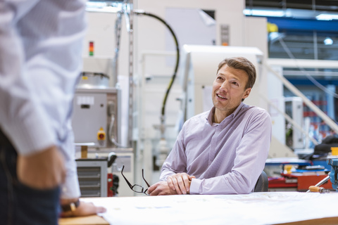 Zwei Männer unterhalten sich in einer Fabrik, lizenzfreies Stockfoto