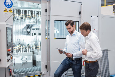 Two men standing at machine in factory looking at tablet - DIGF03452