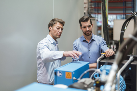 Two men discussing at machine in factory stock photo