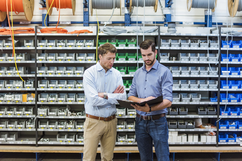 Zwei Männer mit Aktenordner im Lagerraum einer Fabrik, lizenzfreies Stockfoto