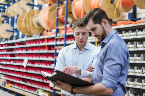 Two men with folder talking in factory storeroom - DIGF03460