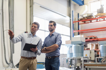 Two men with folder talking in factory storeroom - DIGF03461