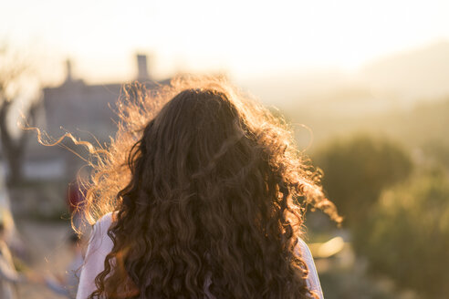 Rückenansicht einer jungen Frau mit langen lockigen Haaren bei Sonnenuntergang - AFVF00115