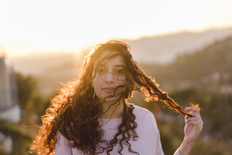 Porträt einer jungen Frau mit langen lockigen Haaren bei Sonnenuntergang, lizenzfreies Stockfoto