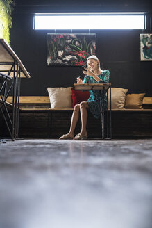 Junge lächelnde Frau mit grünem Kleid sitzt in einem Café und überprüft ihr Smartphone - SBOF01371