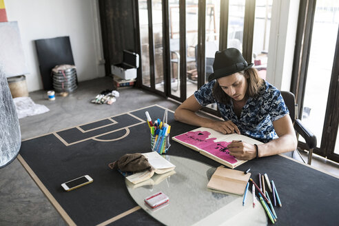 Künstler bei der Arbeit, Zeichnung in einem Notizbuch in seinem Loft-Atelier - SBOF01374