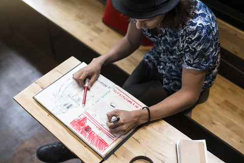 Künstler sitzt im Café und zeichnet in sein Notizbuch, lizenzfreies Stockfoto