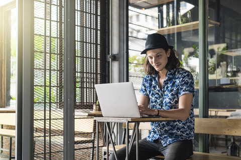 Künstlerin sitzt in einem Café und tippt auf einem Laptop, lizenzfreies Stockfoto