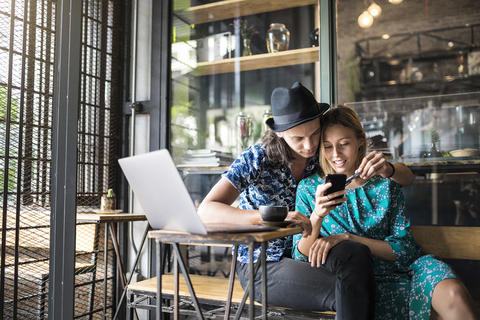 Künstlerpaar sitzt im Café und überprüft das Smartphone der jungen Frau, lizenzfreies Stockfoto