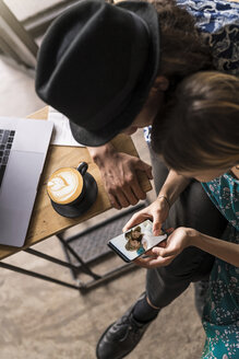 Künstlerpaar sitzt im Café und überprüft das Smartphone der jungen Frau - SBOF01394