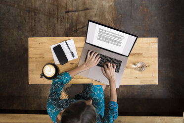 Junge Frau mit grünem Kleid sitzt in einem Café und arbeitet an ihrem Laptop - SBOF01396