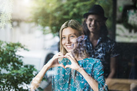 Beautiful young woman making a finger frame heart and smiling at her boyfriend through a window stock photo